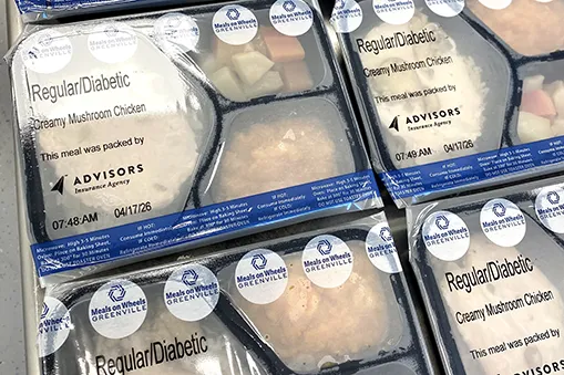 Packaged Meals on Wheels meal trays labeled 'Regular/Diabetic – Creamy Mushroom Chicken,' stacked and ready for delivery